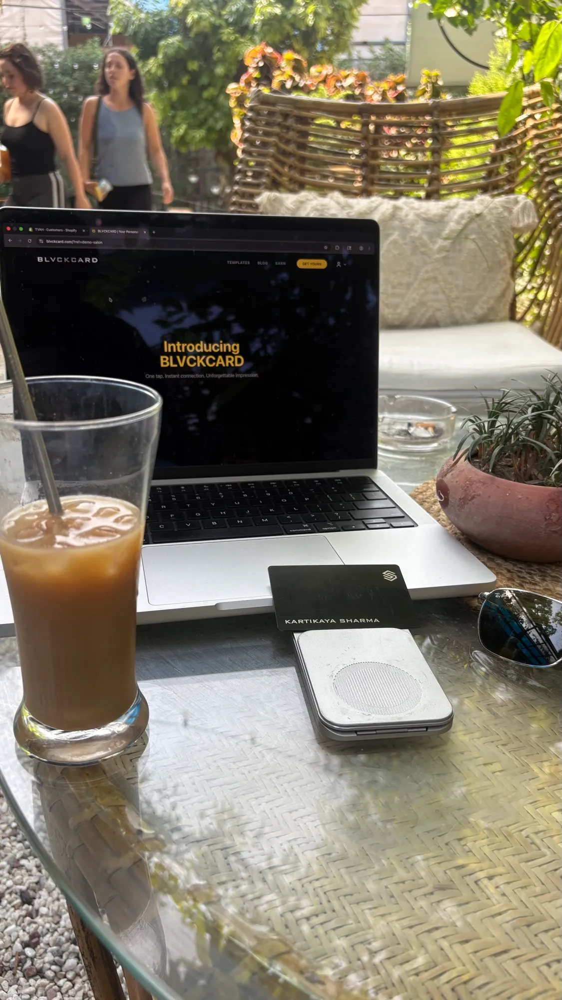 BLACKCARD NFC business card beside a laptop showing the owner's personal website at a cafe